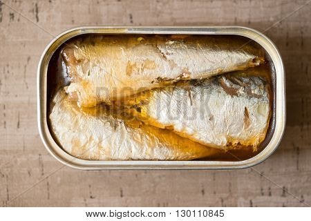 Overhead of an opened can of sardines or herring in oil on wooden surface