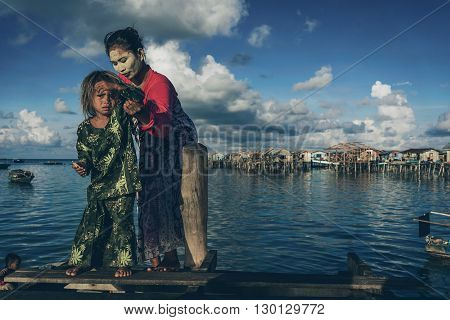 Denawan Island Sabah Malaysia - April 30 2016 : A mother helping her child to stand on a broken wooden bridge. Both were wearing a traditional clothing with the mother had a natural paste on her face as the natural sun block.