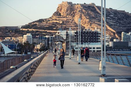 Alicante Spain-February 24 2016: People walking on the Alicante pier. View to the Santa Barbara castle. Castle one of the most well-known landmarks in Alicante and the most visited. Valencian Community Spain