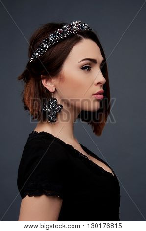 Sexy brunette in black dress with deep cleavage wearing beded crown headpiece and earrings
