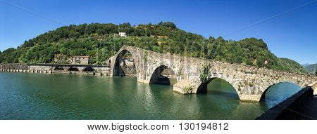 Panoramic view of a unique stone bridge. The medieval Ponte Maddalena or Devils Bridge in Tuscany. Unrecognizable people at the crest of the bridge are included for scale.