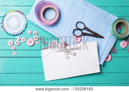 Sewing thread - buttons scissors fabric and empty tag on turquoise wooden background. Selective focus. Scrapbboking. Flat lay. Place for text.