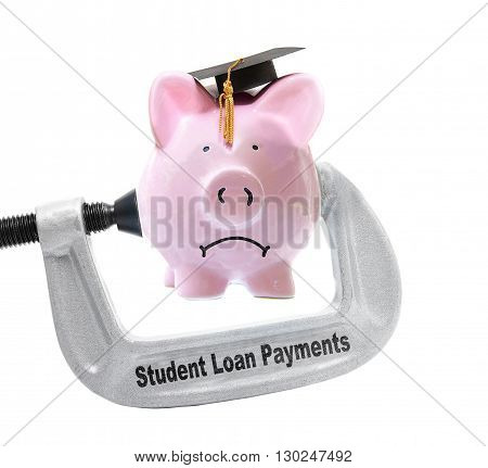 Frowning piggy bank wearing graduation cap being squeezed in a Student Loan Payments vice on white -