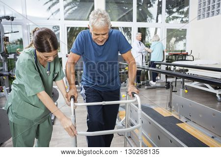Nurse Assisting Senior Man To Walk Using Walker