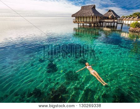 Woman in white bikini swimming in coral lagoon at the resort, Moorea, Tahiti