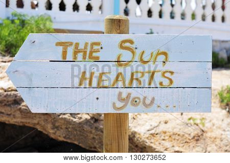 closeup of a white wooden signpost attached to a wooden pole with the text the sun hearts you written in it, pointing the direction towards the beach