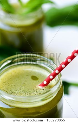 closeup of a detox smoothie served in a glass jar with a red drinking straw patterned with white dots