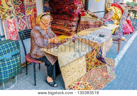 TEL AVIV ISRAEL - FEBRUARY 25 2016: The elderly seamstress makes patchwork rugs from kilim pieces stitched together in the flea market of Jaffa on February 25 in Tel Aviv.