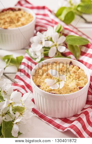 Crumble with strawberry and black currant on a white wooden background with flowering branches of apple trees