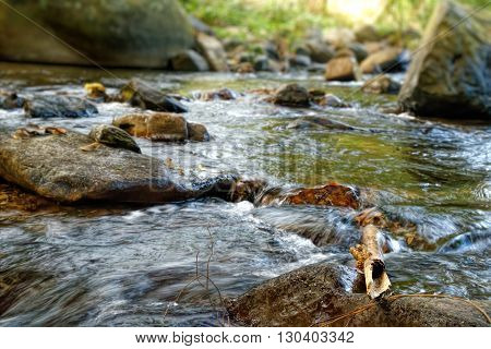 Mountain stream in green forest in sun rays. Khao Sok National Park Surat Thani Province Thailand. Selective focus on a large rock in the foreground.