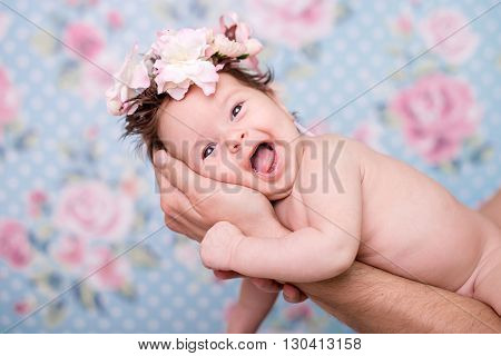 Portrait of a baby girl with a wreath of pink flowers on her head on a light background