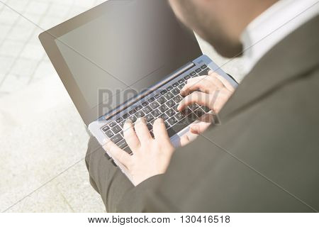 Closeup toned picture of businessman using laptop computer on street incity centre. Freelance man working upon business projects.
