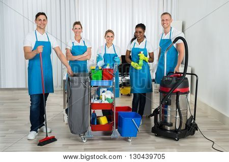 Group Of Happy Cleaners Standing With Cleaning Equipments In Office