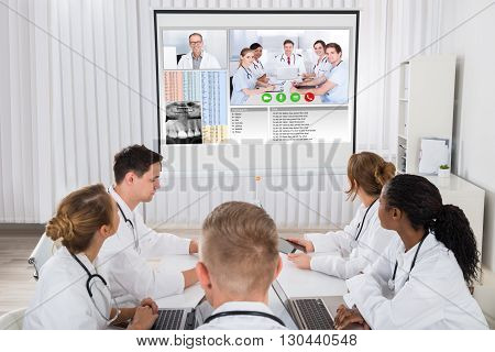 Group Of Doctors Videoconferencing With Male Doctor In Hospital