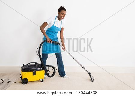 Young Happy Female Janitor Using Vacuum Cleaner On Floor At Office