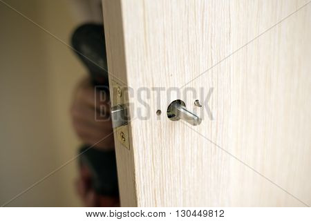 Installation of door lock using a screwdriver to. Carpenter at lock installation with electric drill into wood door.