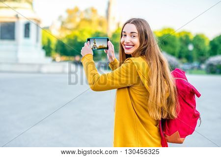 Young female tourist with back pack photographing with smart phone Austrian national hero monument on Hendel square.