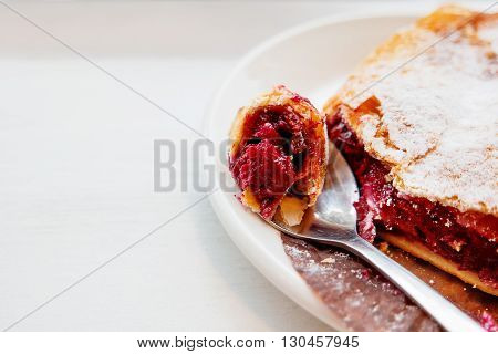 Cherry strudel on a saucer with a spoon. Piece of fresh tasty dessert with berries.