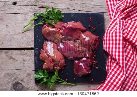 Raw chicken liver on slate board with towel on aged wooden background. Garnished with herb parsley and red pepper. Food ingredient. Selective focus.