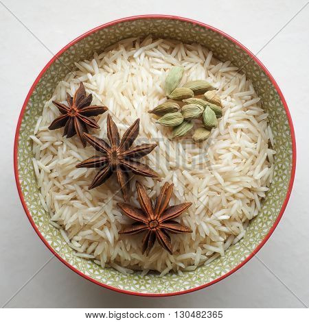 Uncooked long grain basmati rice in a colorful ceramic bowl with star anise and cardamom pods.