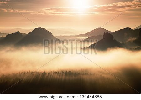 Distant Mountain Range And Heavy Clouds Of Colorful  Mist Above Deep Valleys