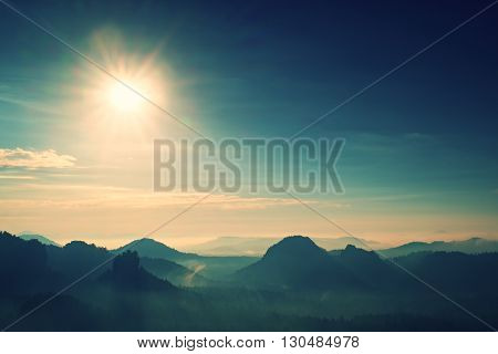 Distant Mountain Range And Heavy Clouds Of Colorful  Mist Above Deep Valleys
