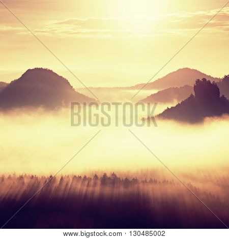 Distant Mountain Range And Heavy Clouds Of Colorful  Mist Above Deep Valleys
