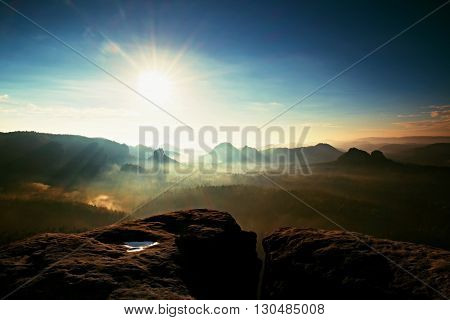 Distant Mountain Range And Heavy Clouds Of Colorful  Mist Above Deep Valleys