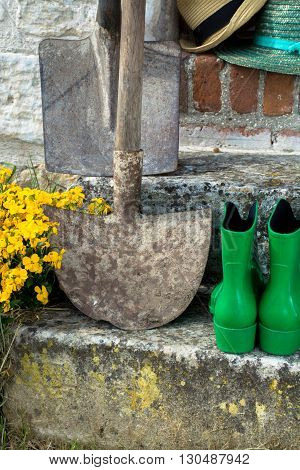 Garden equipment - rubber boots schovels and srtaw hats in sunny day on old stone wall background