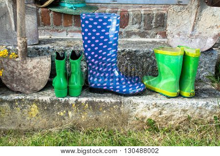 Garden equipment - rubber boots schovels and srtaw hats in sunny day on old stone wall background