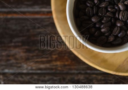 Top view of coffee beans in a cup on wooden background. For insert text design in advertising.