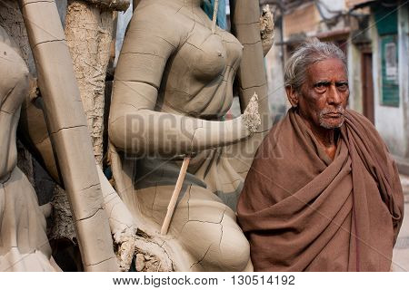 KOLKATA, INDIA - JAN 15, 2013: Senior asian man stands near the woman sculpture at Kumartuli artistic area on January 15, 2013 in India. Populat. of Kolkata is 4.5 million out 25 million are males