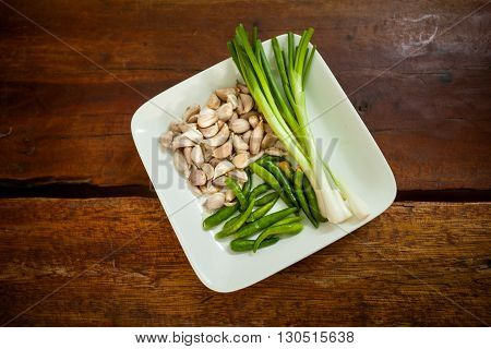 Fresh spring onion bird eye green chilli and baby garlic on plate. Set of traditional thai spices.