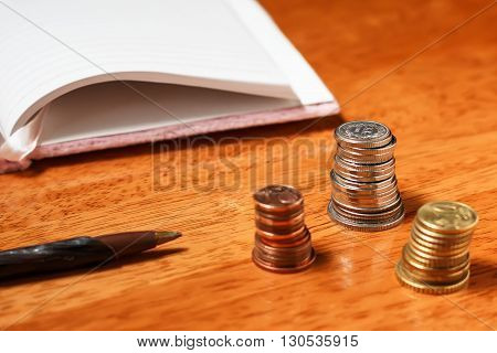 Stacks of coins with pencil and blank open notebook in the background