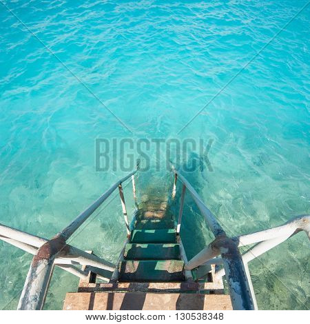Old vintage metal wooden stairs leading to blue turquoise sea water from beach. Beautiful summer day. Swimming pool with grunge retro stairs on the ocean coast. Top View.