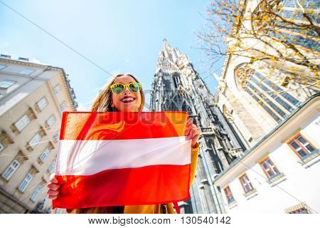 Young smiling woman holding austrian flag with St. Stephen's Cathedral on the background in Vienna