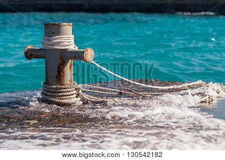 Rusty mooring bollard with ship ropes and  clear turquouse sea ocen water on background.