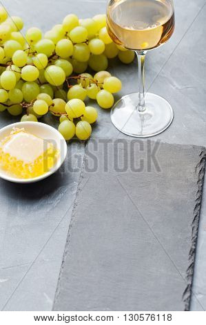 Glass of white wine and assorted cheese with grape on a stone and slate background Copy space