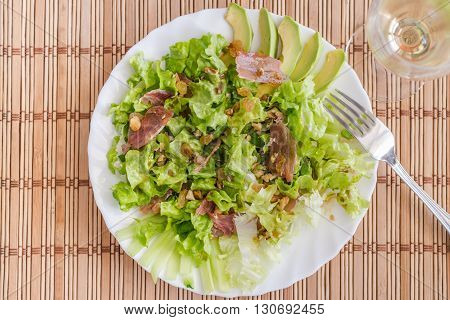Green mix salad plate with avocado prosciutto raisins and pecans over bamboo mat