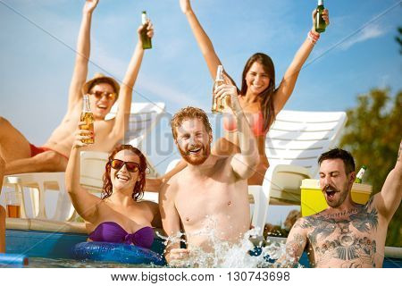 Cheerful youngsters group toasting with hands up with bottles of refreshing drink in open piscine