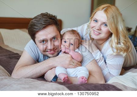 Beautiful happy couple and their baby relaxing in a bed together.