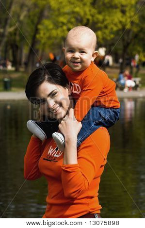 Baby and mother are having fun togather in the citypark on a sunny spring afternoon. They are wearing a similar orange T-shirt.