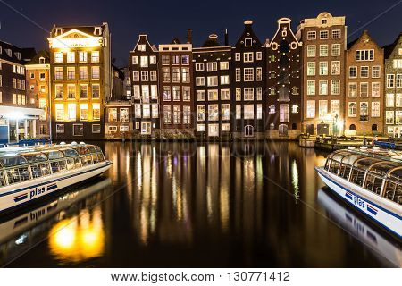 AMSTERDAM NETHERLANDS - 16TH FEBRUARY 2016: Old Buildings along the Damrak in Amsterdam at night. Boats and reflections can be seen.