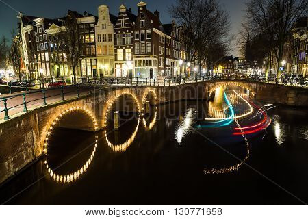 A view of the bridges at the Leidsegracht and Keizersgracht canals intersection in Amsterdam at dusk. The trail from a boat can be seen.