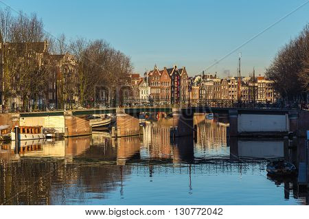 AMSTERDAM NETHERLANDS - 16TH FEBRUARY 2016: A view along the Waalseilandgracht Canal in Amsterdam at twilight. Building boats and people can be seen.