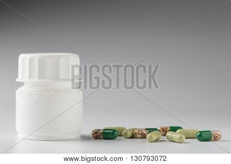 Medicine white bottle and various colorful medical pills and capsules on gray background