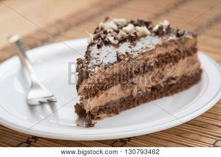 Slice of fresh delicious chocolate cake on a plate garnished with nuts and a small fork.