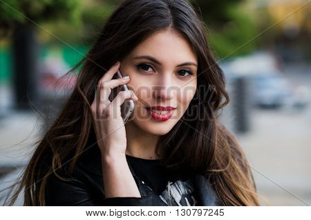 Portrait of a beautiful woman with a perfect white smile talking on the mobile phone outdoor