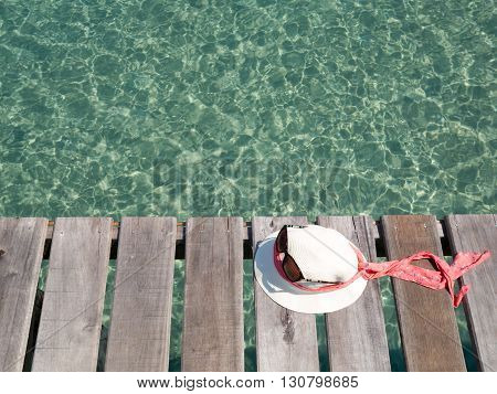 White lady hat and sunglass on wooden slat floor against with green crystal sea water surface ripple and sun reflection. Water background. Ocean water texture.