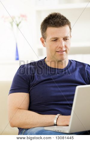 Mann auf Sofa zu Hause sitzen und Laptopcomputer verwenden.